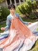 A woman in a pink and blue hanbok sitting on the grass.