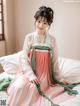 A woman in a pink and green hanbok sitting on a bed.