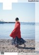 A woman in a red sweater is walking on the beach.