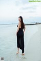 A woman in a black dress standing on a beach.