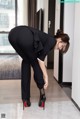 A woman in a black suit bending over to pick up her shoes.