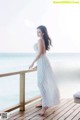 A woman in a white dress standing on a wooden deck.