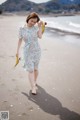 A woman walking on a beach holding a pair of yellow shoes.