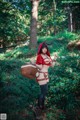 A woman dressed as a red riding hood holding a basket in the woods.